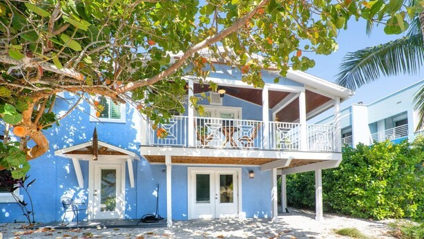 A two-story house with a balcony, a covered porch, and a gravel driveway. - Beachwalker Apartment:  Duplex within 100 steps to the sand. (Holmes Beach)