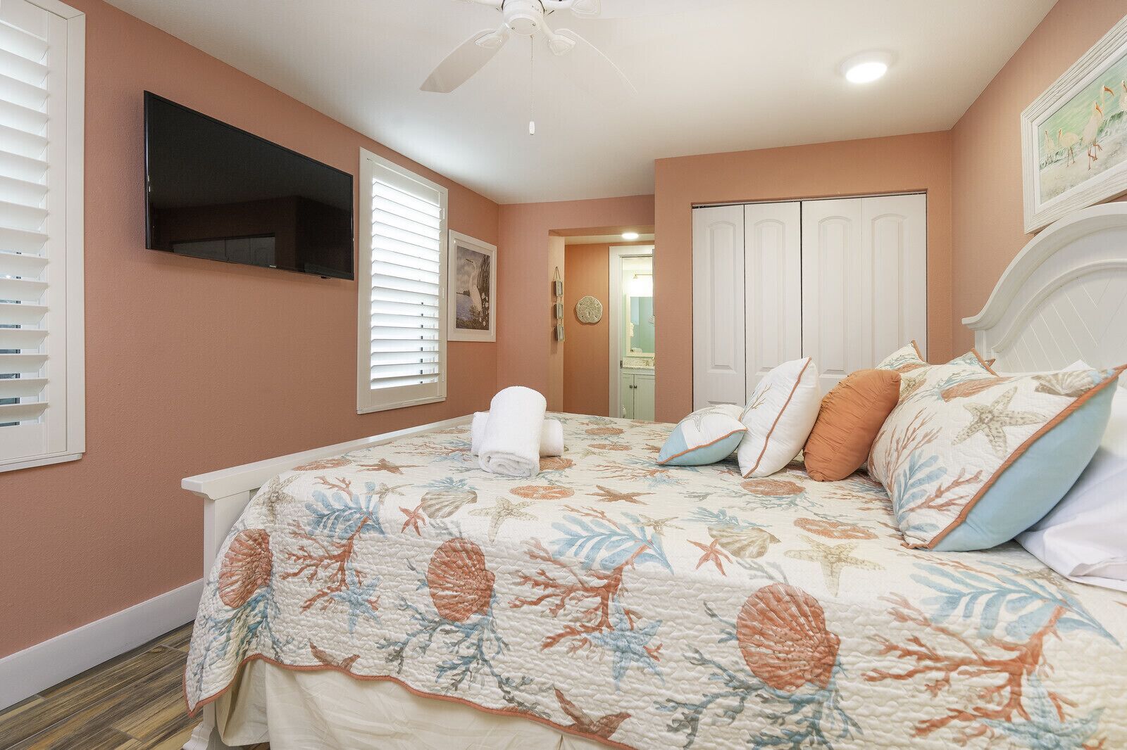 A bedroom with a bed, a ceiling fan, a TV, and a door leading to another room.