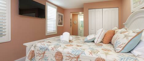 A bedroom with a bed, a ceiling fan, a TV, and a door leading to another room.