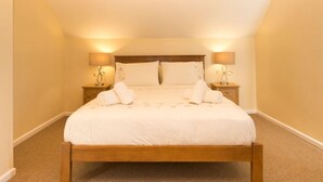 A neatly made bed in a room with a sloped ceiling, two bedside tables with lamps, and a carpeted floor. - Mallow Cottage (Swanage)