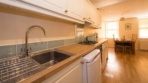 A kitchen with white cabinets, a stainless steel sink, a wooden countertop, a gas stove, and a dishwasher. - Mallow Cottage (Swanage)