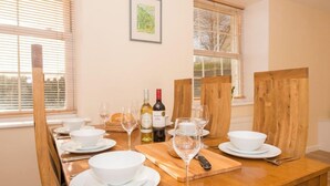 A dining table set for four with white plates, bowls, and wine glasses, a bottle of wine, and a cutting board with bread. - Mallow Cottage (Swanage)