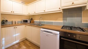 A kitchen with white cabinets, a microwave, a sink, a gas stove, and a dishwasher. - Mallow Cottage (Swanage)