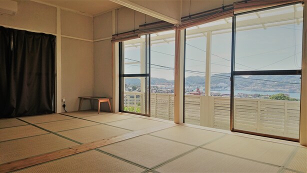 A room with tatami flooring, a sliding door with a view of a cityscape, and a small stool. - The Sloope Nagasaki (Nagasaki)