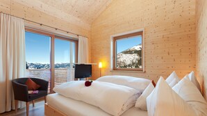 A wooden cabin room with a bed, a chair, a TV, and large windows offering a mountain view. - Biohotel Mattlihüs (Bad Hindelang)