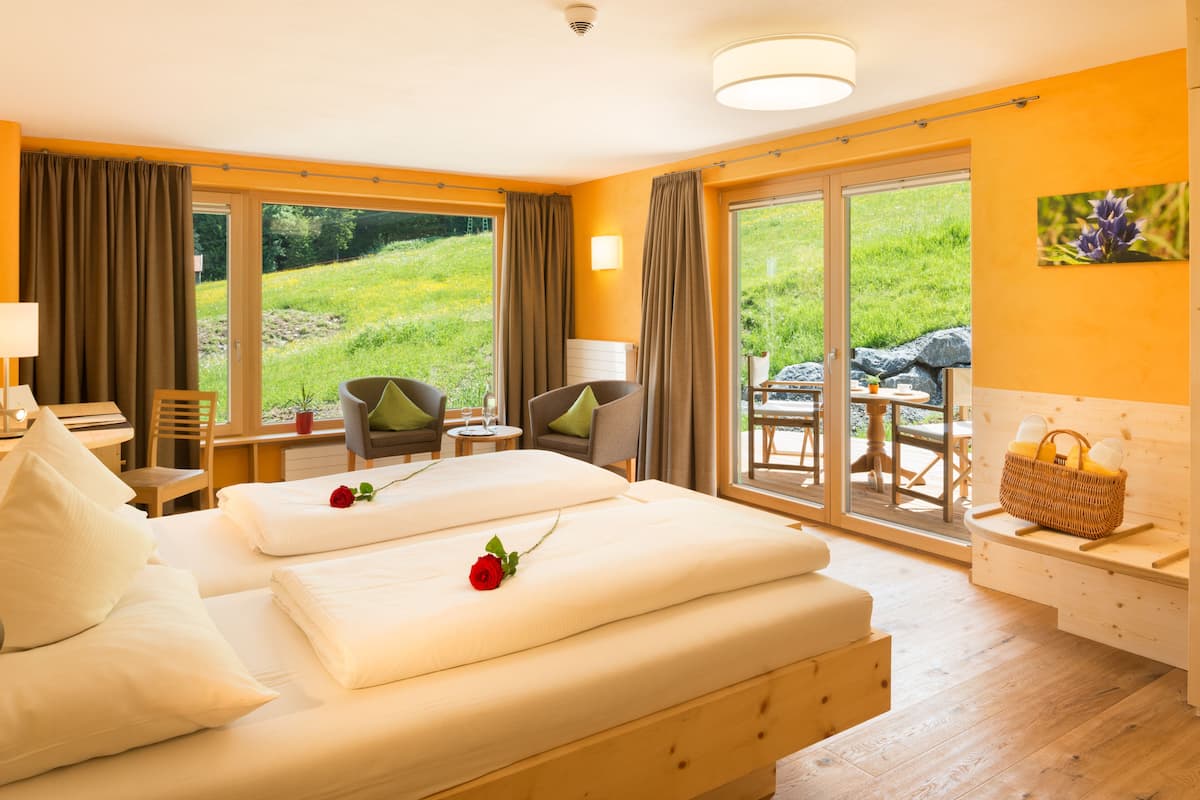 Een hotelkamer met een groot bed, twee stoelen, een tafeltje, een bank en uitzicht op een grasveld door de ramen.