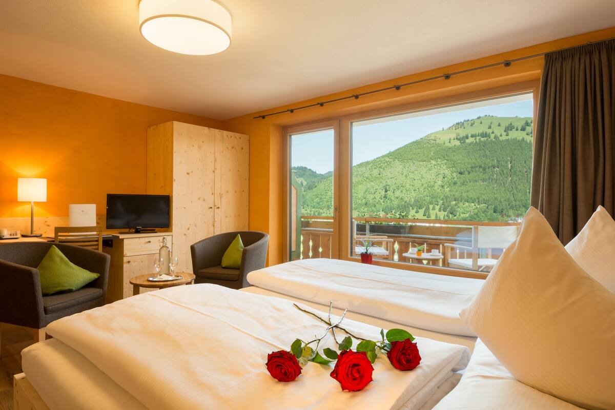 Een hotelkamer met twee bedden, een televisie, een bureau en een balkon met uitzicht op de bergen.