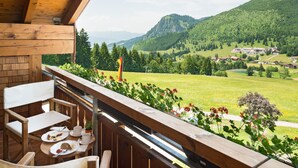 A balcony with wooden furniture, a table with plates and cups, and a view of a green valley with houses and mountains. - Biohotel Mattlihüs (Bad Hindelang)