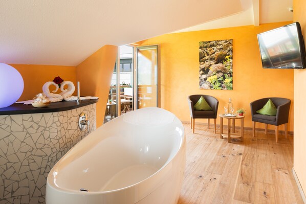 Un baño moderno con una bañera independiente, una pared de mosaicos y una zona de estar con dos sillones y una mesita.