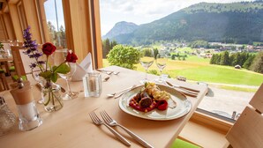 A dining table with a meal, utensils, and a vase with flowers. - Biohotel Mattlihüs (Bad Hindelang)