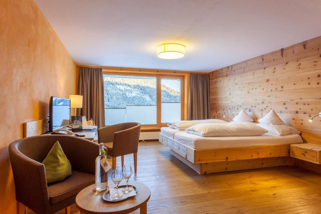 Habitación de hotel con cama, escritorio, silla y mesa con vasos y una botella.