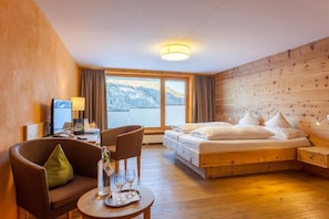 A hotel room with a bed, a desk, a chair, and a table with glasses and a bottle. - Biohotel Mattlihüs (Bad Hindelang)