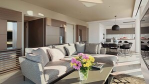 A modern living room with a sofa, a coffee table with a vase of flowers, and a dining area with chairs and a table. - Sunlight Acropolis Loft (Athens)