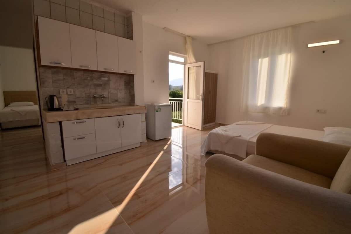 A modern hotel room with a kitchenette, a sofa, a bed, and a balcony with a view.