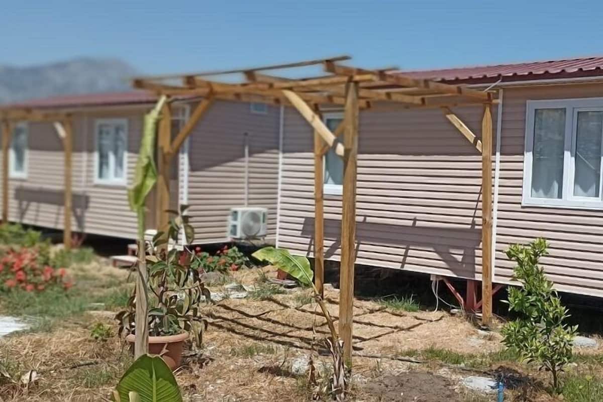 A row of mobile homes with wooden exteriors and metal roofs, each with a small porch and a window.