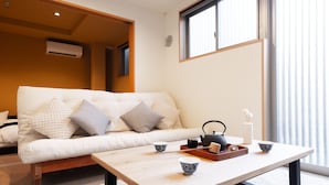 A modern living room with a sofa, a coffee table, and a window with blinds. - Temple Hotel Shoden-ji (Tokyo)