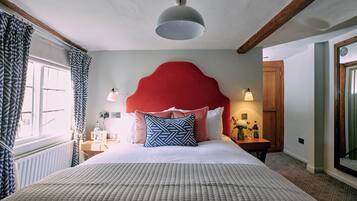 A bedroom with a large bed, a red headboard, and a window with patterned curtains.