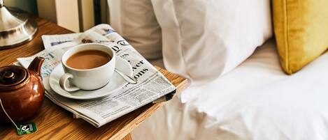 Una mesita de noche de madera con una taza blanca de café, una tetera y un periódico.