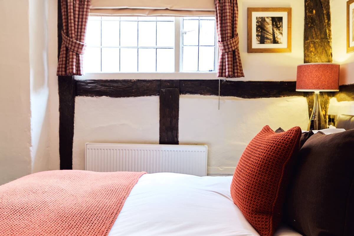 A bedroom with a large bed, a radiator, a window with curtains, and a lamp.