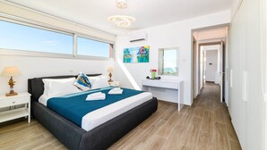 A modern hotel room with a large bed, a desk, and a view of the sky. - Infinity View Villa - Charming Ayia Thekla Getaway (Ayia Napa)