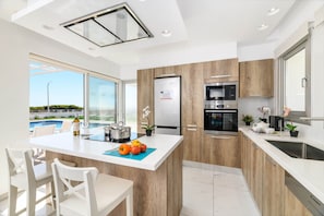 A modern kitchen with a large island, built-in appliances, and a view of a swimming pool. - Infinity View Villa - Charming Ayia Thekla Getaway (Ayia Napa)