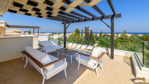 Eine Terrasse mit weißer Möbel, einer Pergola und Blick auf das Meer.
