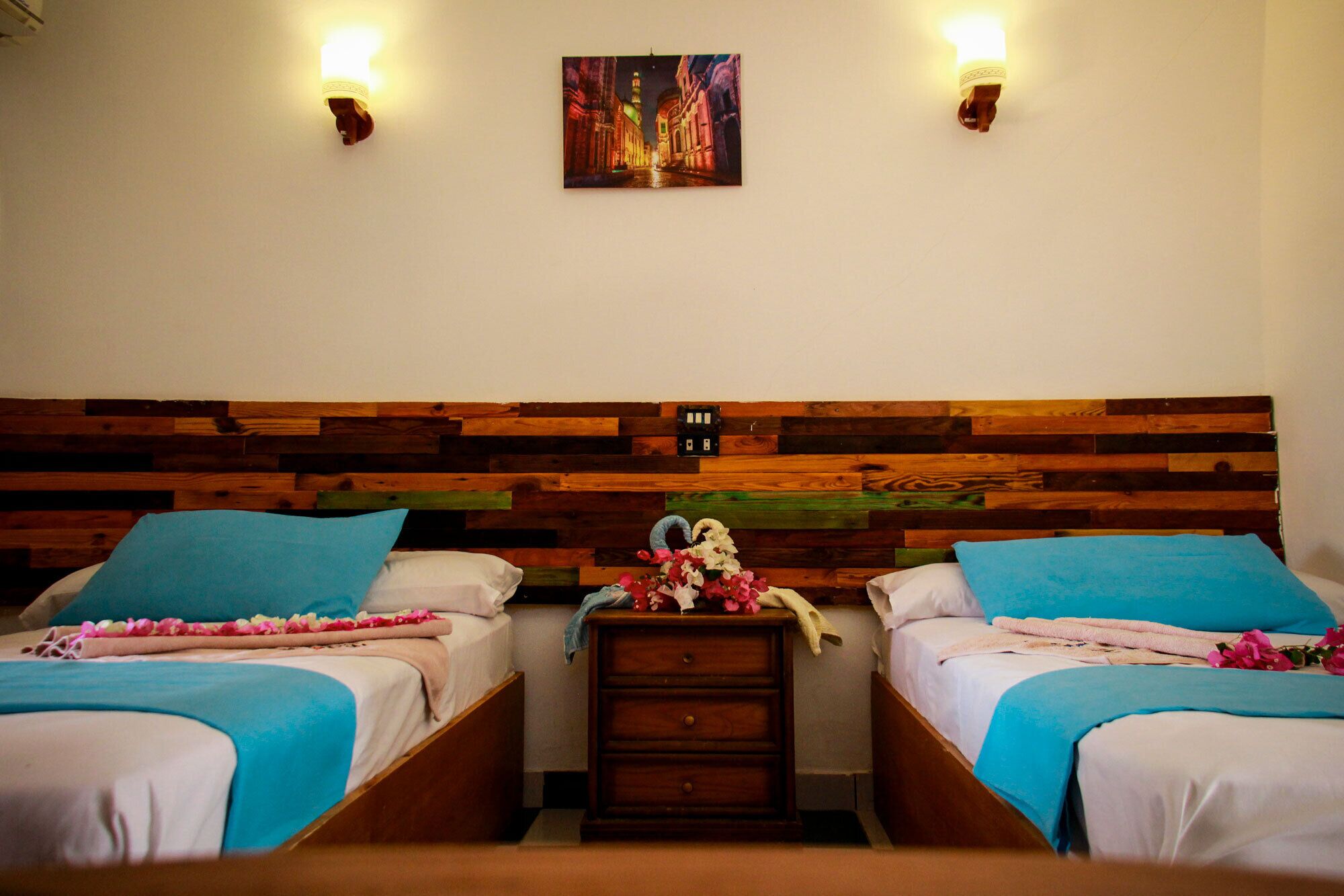 A room with two beds, wooden headboard, nightstands, and wall-mounted lights.