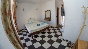 A room with a checkered floor, a bed with a white mattress, a wooden headboard, a mirror, and a coat rack. - Penguin Village Dahab (Dahab)