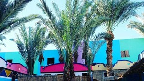 A colorful building with a blue and pink facade, surrounded by palm trees. - Penguin Village Dahab (Dahab)