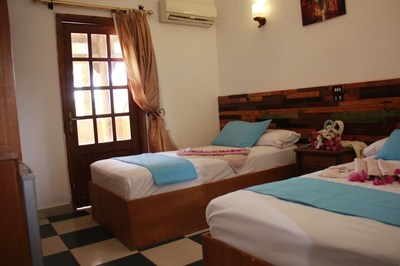 A hotel room with two beds, a checkered floor, a wooden headboard, and a window with curtains.