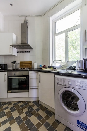 A kitchen with a built-in oven, a microwave, a washing machine, and a window providing natural light.