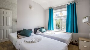 A hotel room with two beds, a window with curtains, a bedside table, and a wall-mounted clock. - My City Chic St. Pancras Apartment (London)