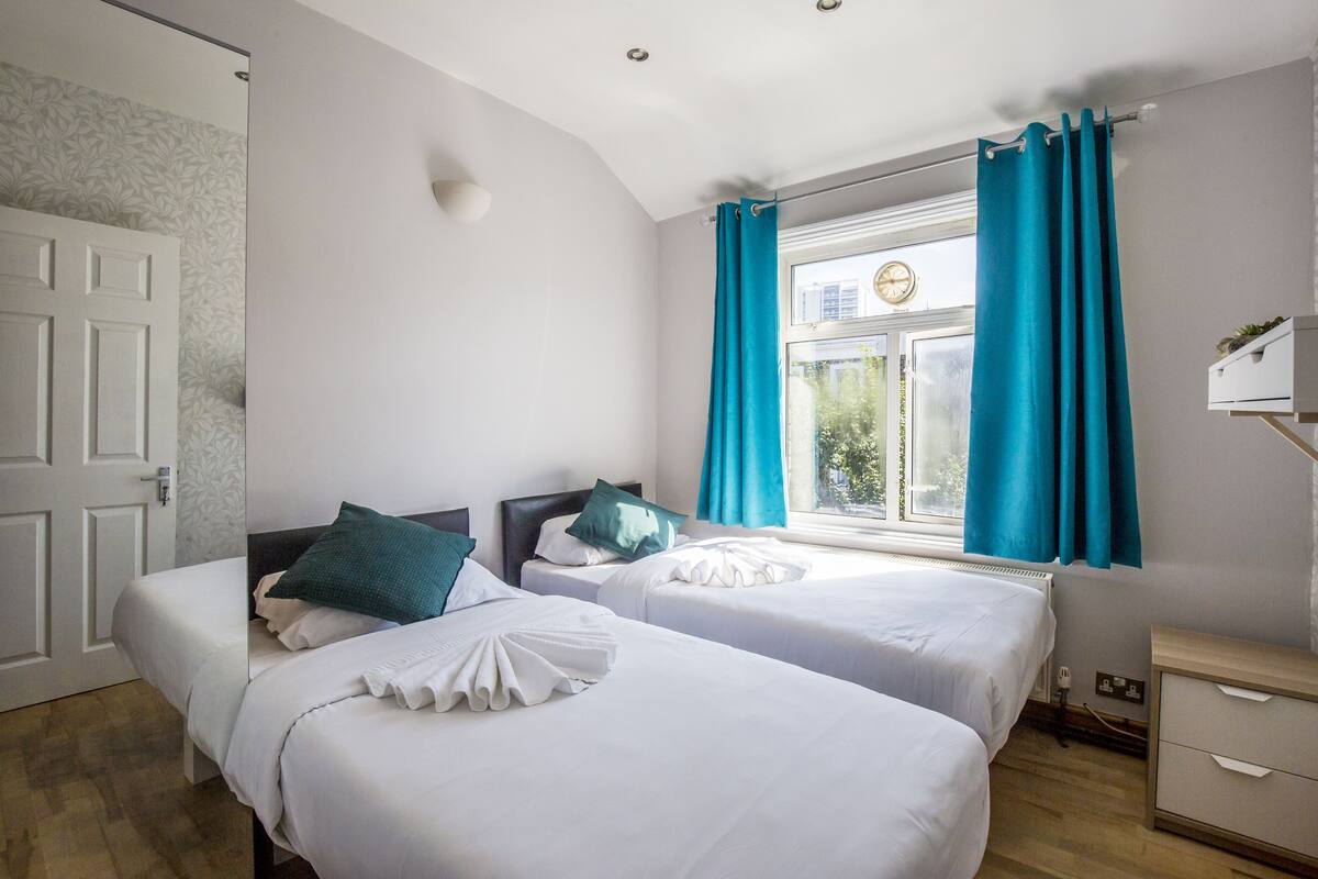 Une chambre d’hôtel avec deux lits, une fenêtre avec des rideaux, une table de chevet et une horloge fixée au mur.