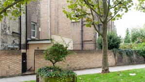 A brick building with a small tree in a planter, a gated entrance, and a grassy area with fallen leaves. - My City Chic St. Pancras Apartment (London)