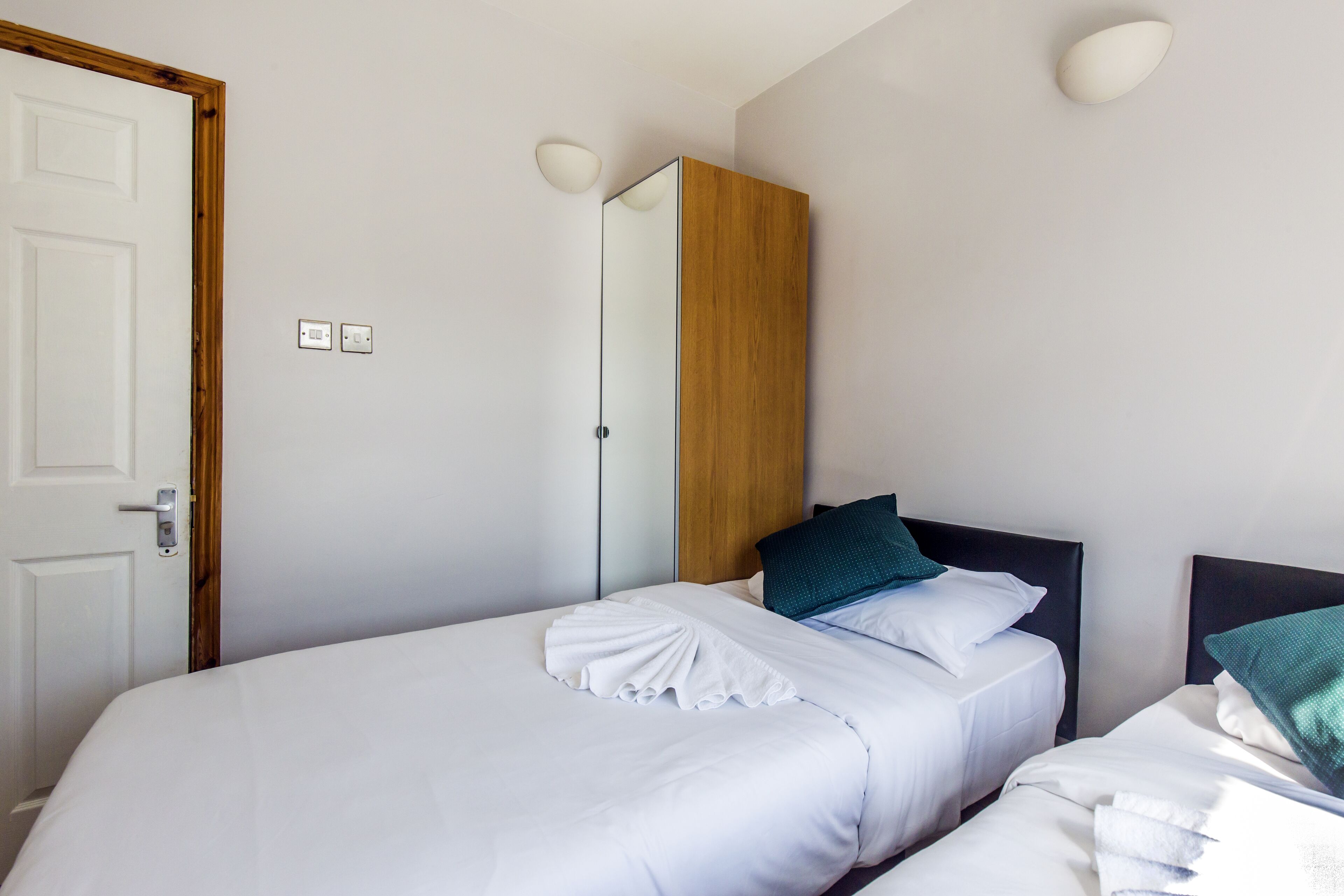 A hotel room with two beds, a wooden wardrobe, and a white door.
