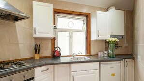 A kitchen with white cabinets, a gas stove, a red kettle, and a window with a view. - My City Chic St. Pancras Apartment (London)