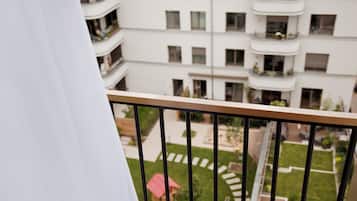 Une vue depuis un balcon donnant sur un immeuble d’habitation doté de nombreux balcons et d’un petit jardin.