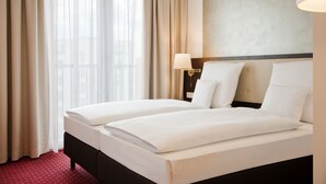 Une chambre d’hôtel avec un lit double, une table de chevet avec une lampe et une vue sur l’extérieur à travers des rideaux transparents.