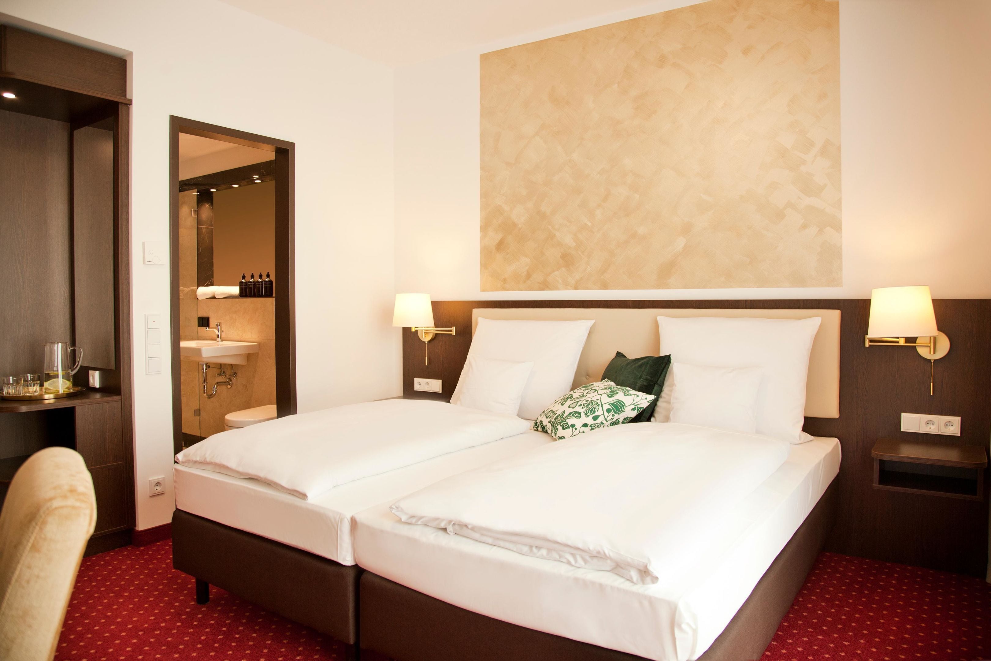 A hotel room with two beds, a bathroom, and a desk with a chair.