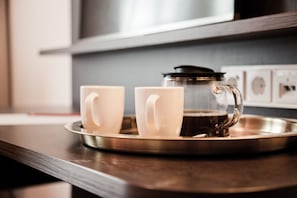 Una bandeja de acero inoxidable con dos tazas de cerámica blanca y una jarra de café de vidrio sobre una encimera de madera.
