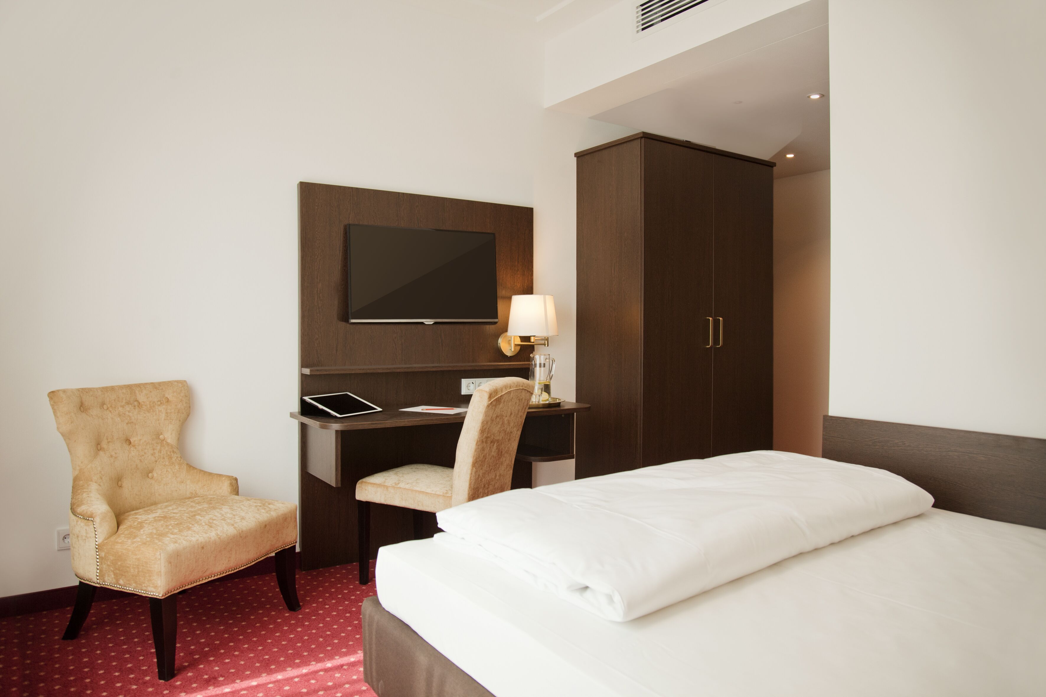 A hotel room with a bed, a desk, a chair, a television, and a wardrobe.
