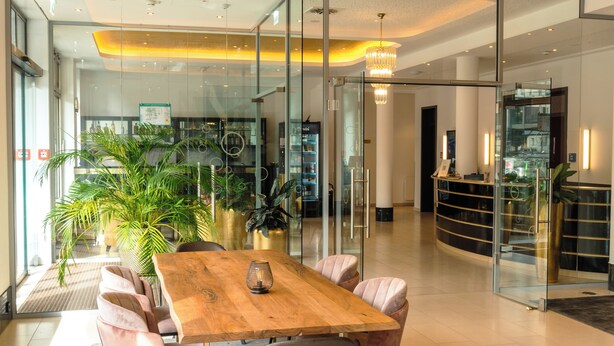 Un intérieur moderne avec une table à manger en bois, des chaises rembourrées et une grande plante en pot.