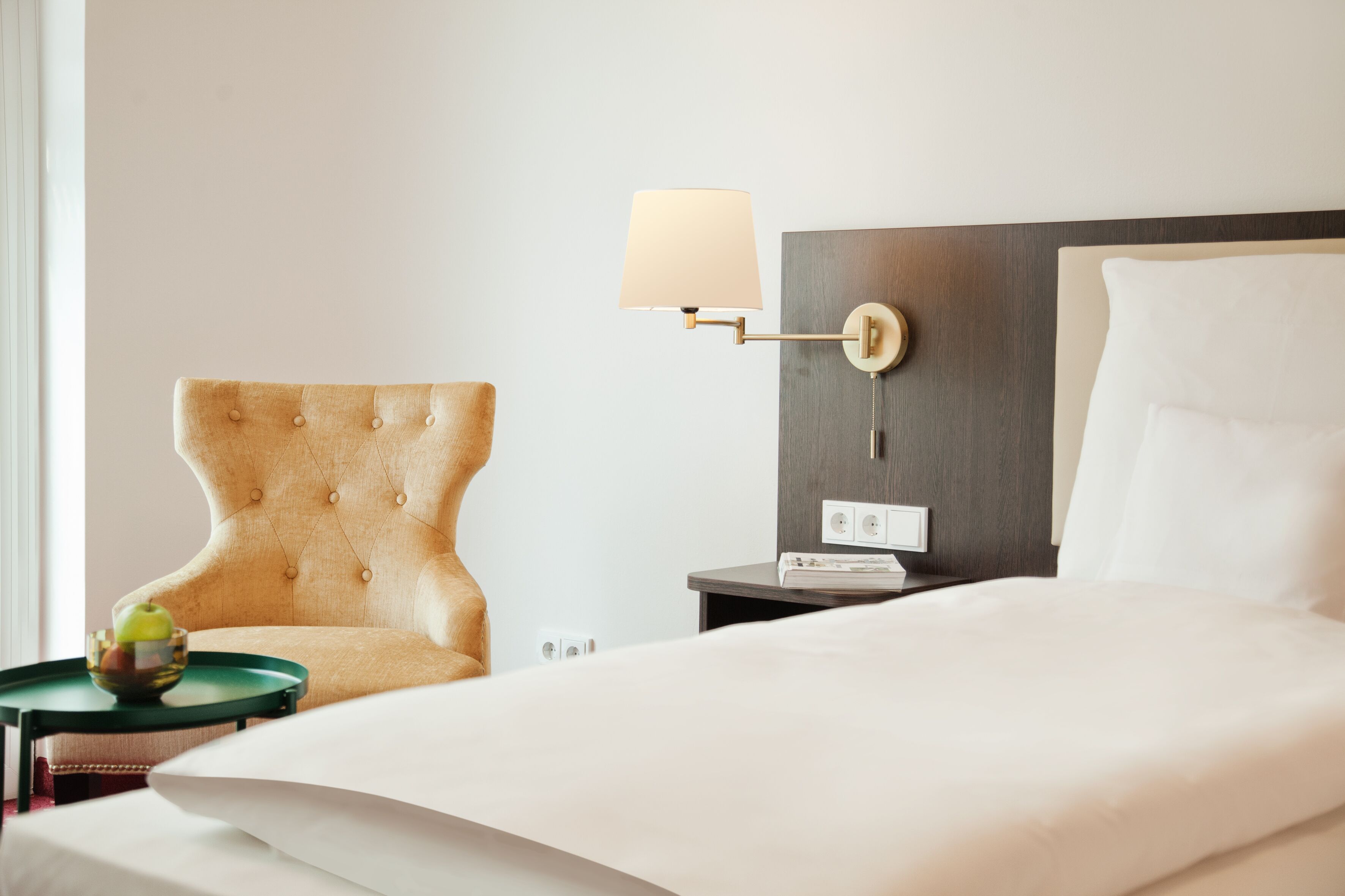 Ein Hotelzimmer mit einem Bett, einem Sessel, einem Nachttisch mit Lampe und einem kleinen Tisch mit einer Obstschale.