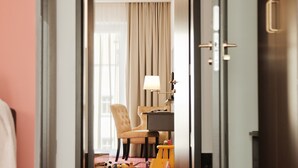 Un couloir d’hôtel avec un tapis rouge, une chaise, un bureau avec une lampe et une porte.