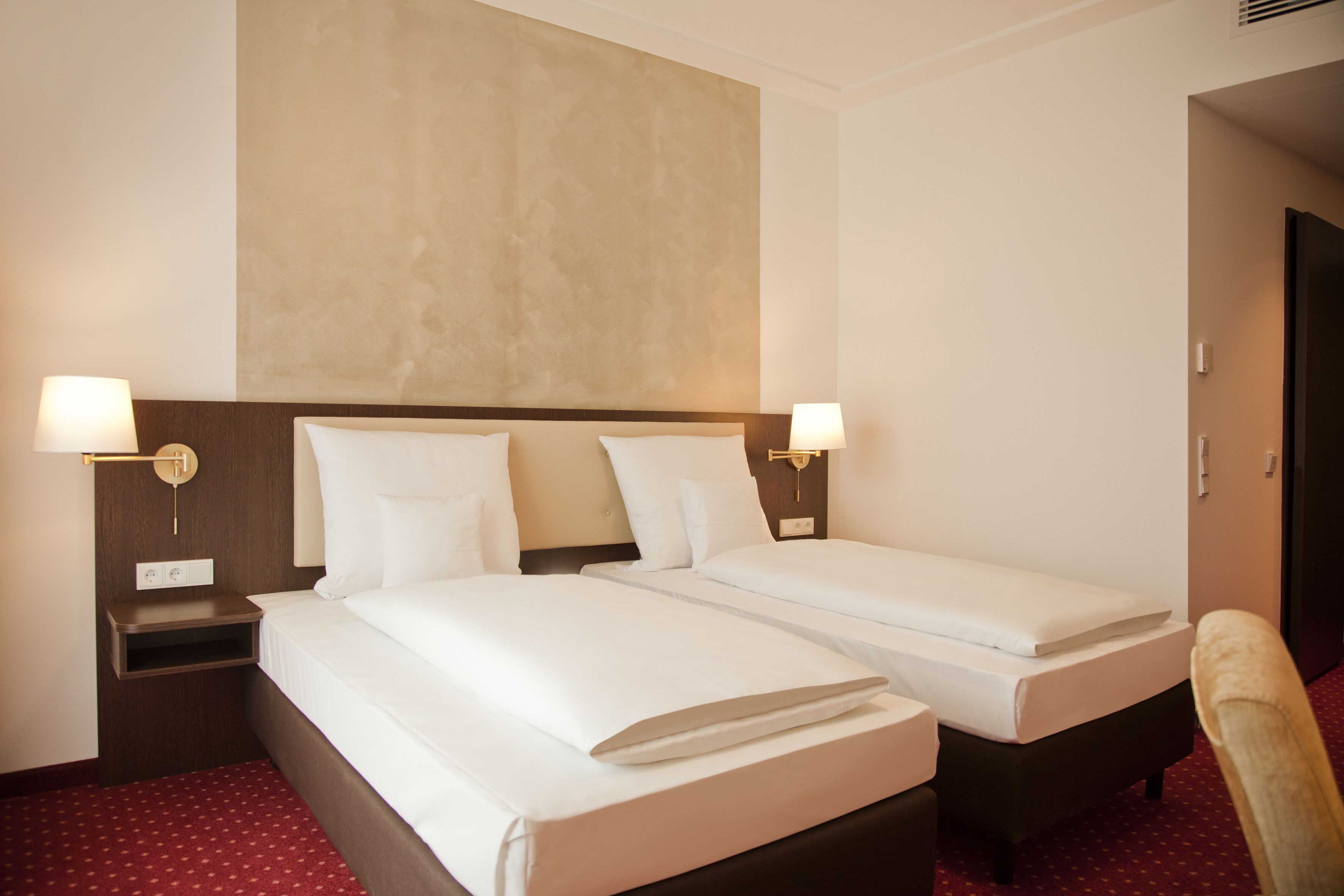 A hotel room with two single beds, a nightstand, a lamp, and a chair.