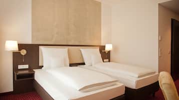 A hotel room with two single beds, a nightstand, a lamp, and a chair.