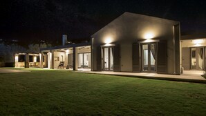 Ett modernt hus med en täckt uteplats, en gräsmatta och en stjärnklar natthimmel.