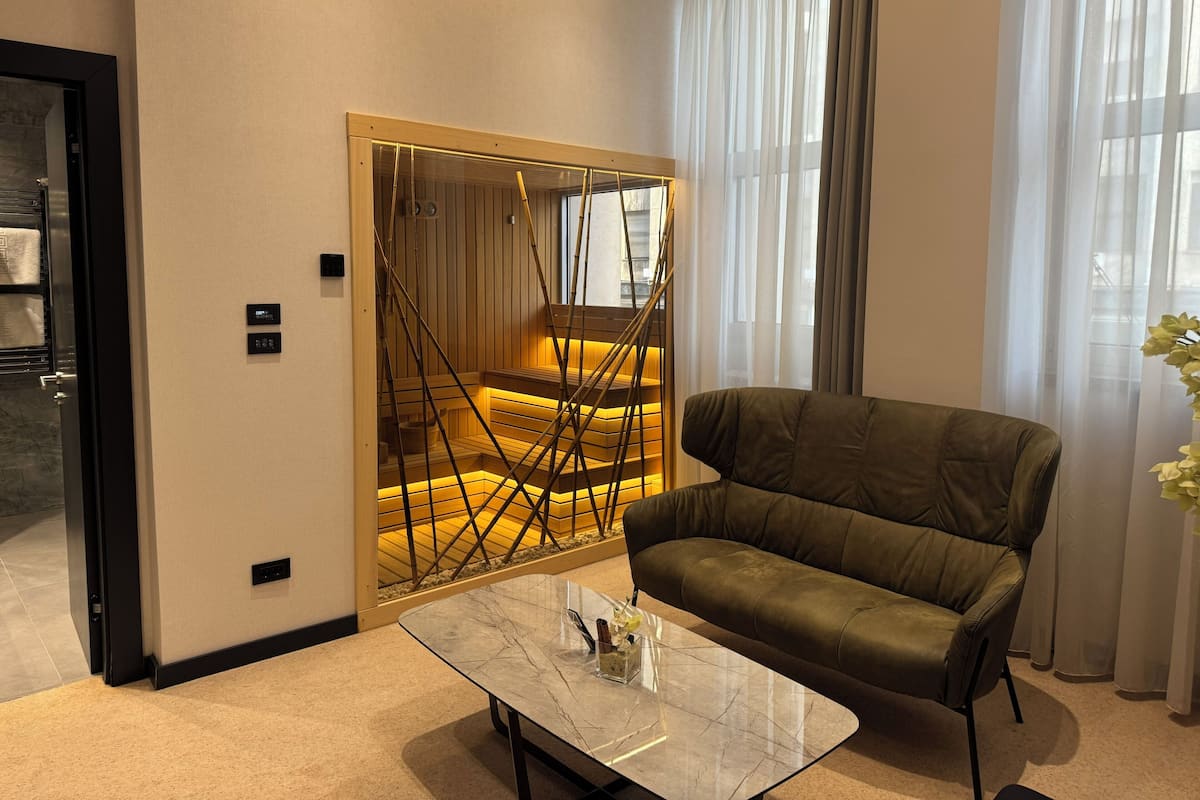A modern living room with a leather sofa, a marble coffee table, a wooden staircase with a glass railing, and a large window with sheer curtains.