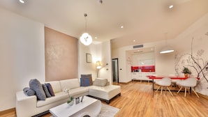 A modern living room with a sofa, coffee table, and dining area with chairs and a red table. - Atera Business Suites (Belgrade)