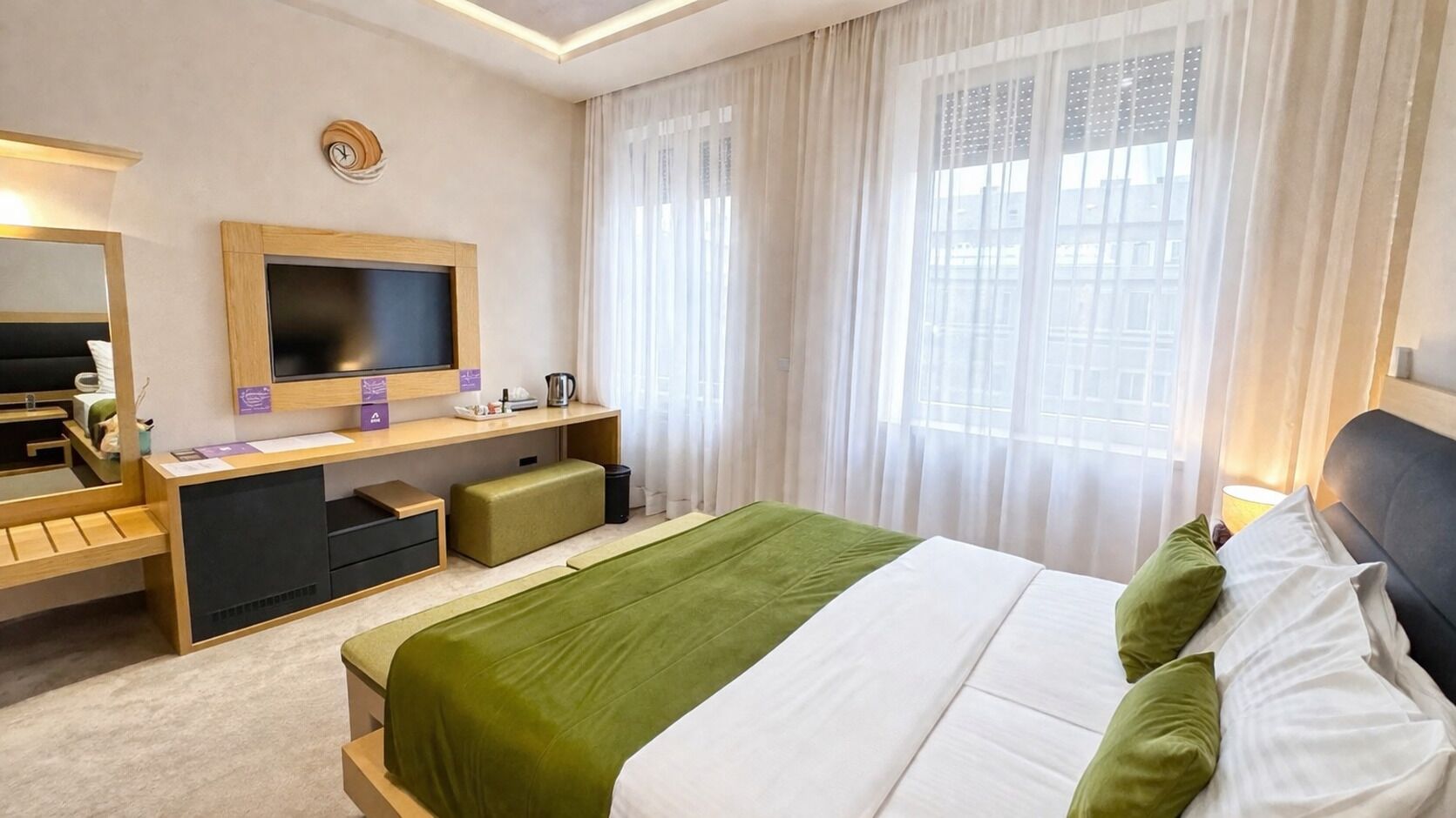A hotel room with a bed, a desk, a chair, a mirror, a television, and a window with curtains.